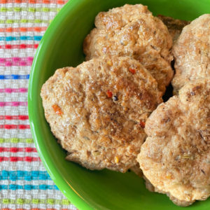 Low Sodium Sausage patties placed in a green bowl a top a colorful striped kitchen towel